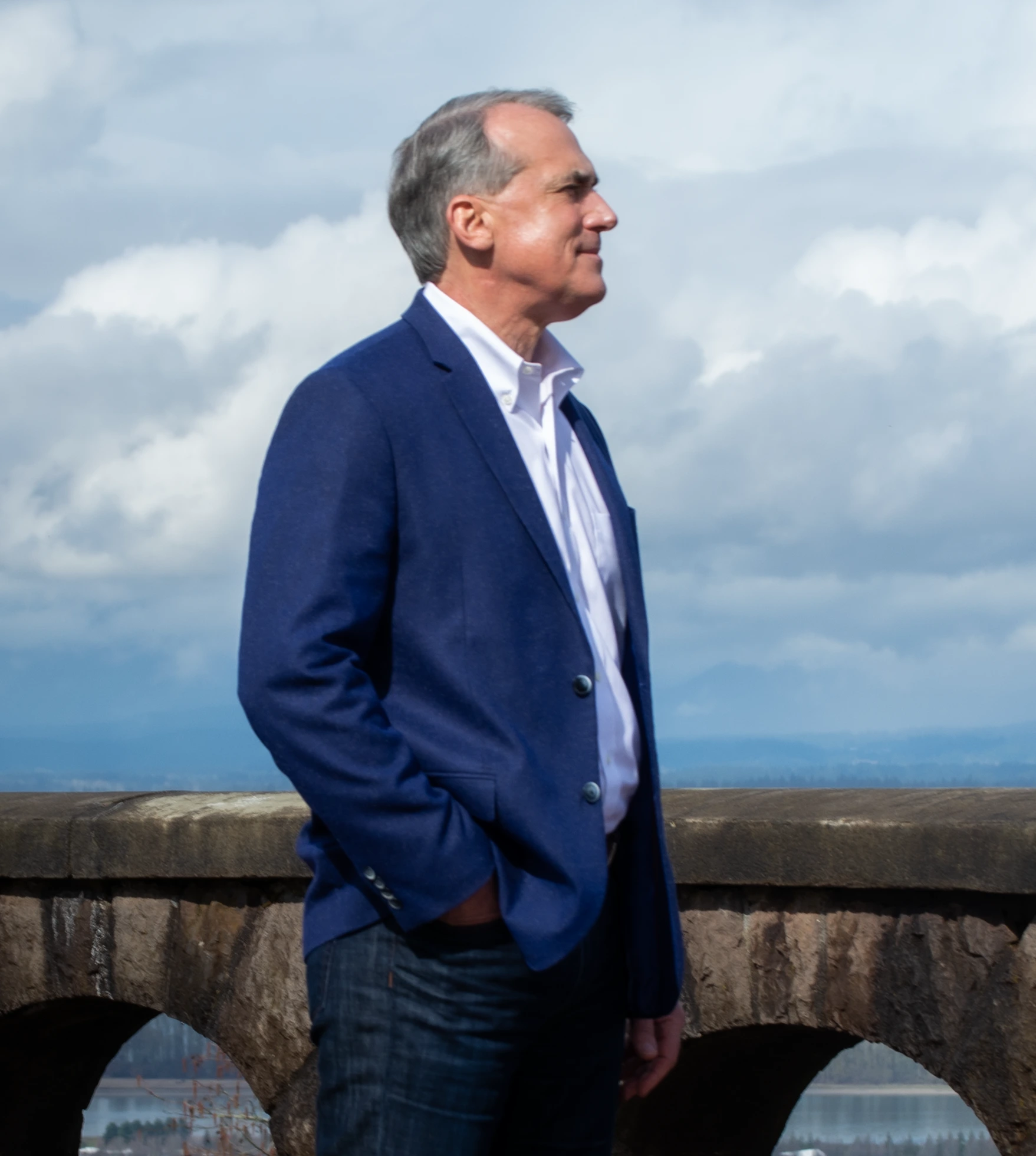 Anthony Metten in a blue blazer beside a stone terrace, looking toward the horizon